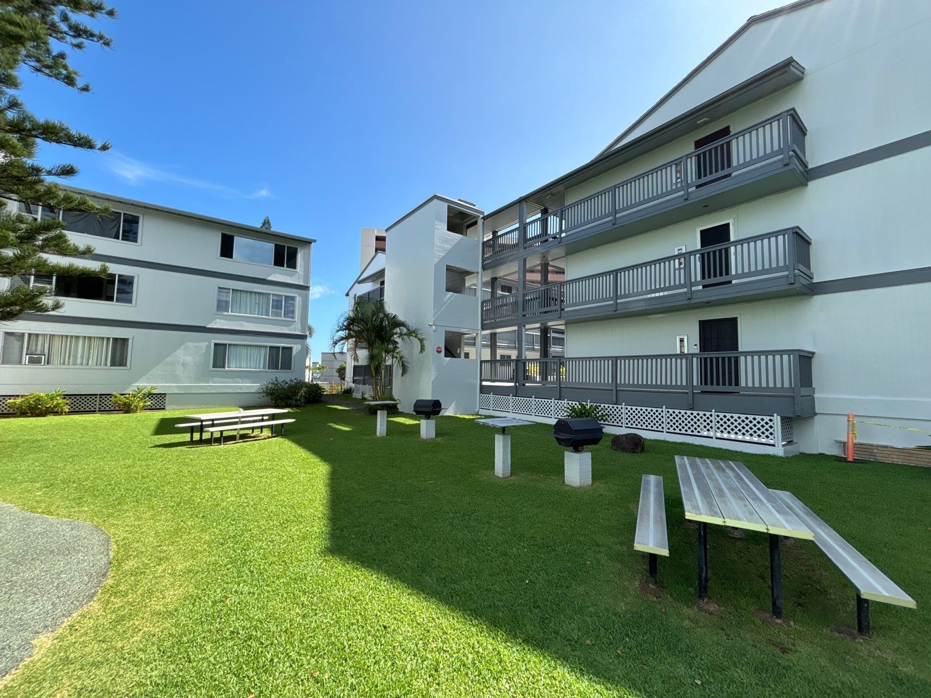 Kāneʻohe condo buildings in pale gray with charcoal railings around a lawn with picnic tables