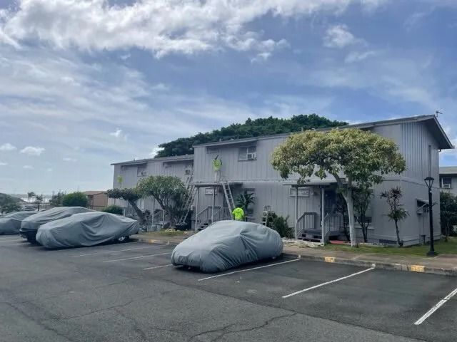 Painters on ladders at a condo building while the residents’ cars sit under covers