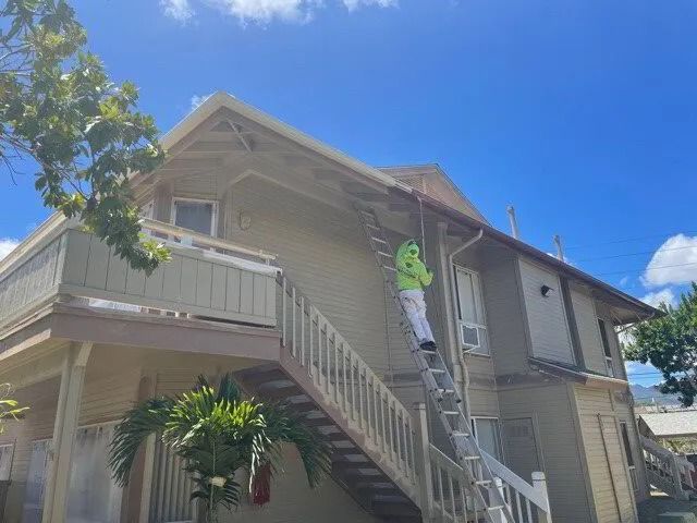 A painter in a green hood on a ladder beside a townhouse’s outside stairs