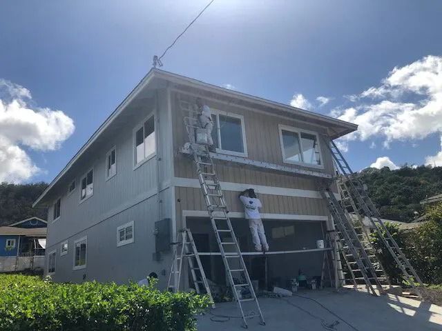 Two painters on ladders at the front of a gray two-story house