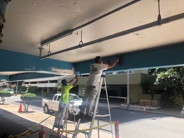 Two painters on ladders patching the ceiling of a building’s drive-through