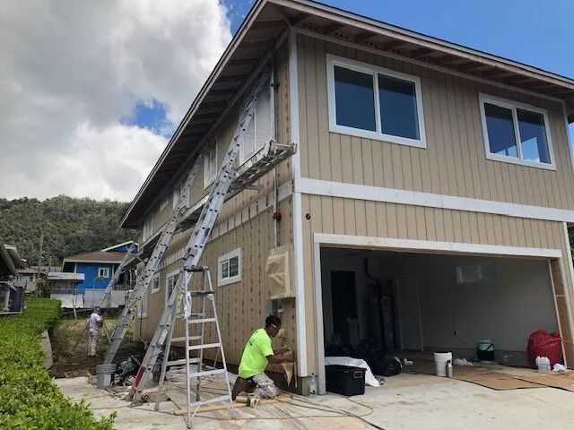 A crew on ladders and at the garage wall, prepping a tan two-story home’s siding