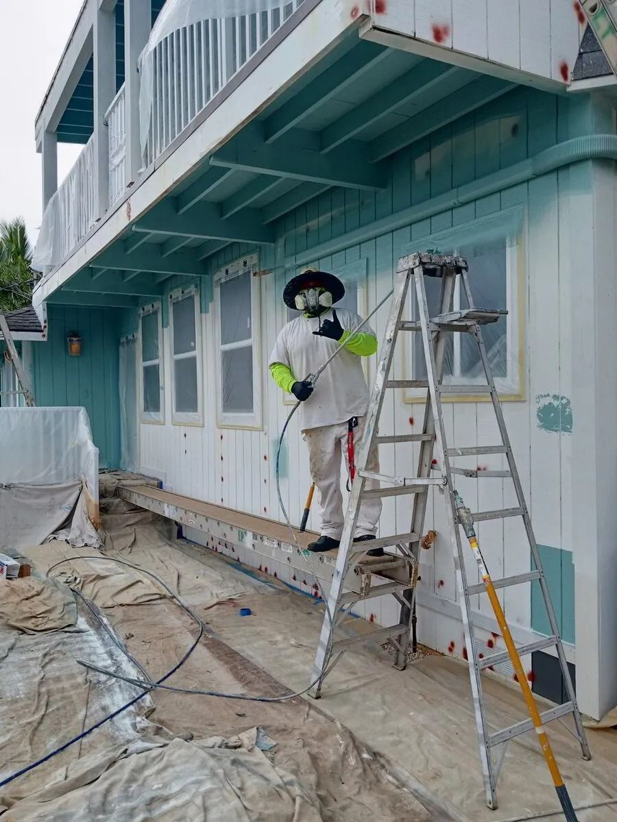 An Emerald Painting painter in a respirator and full coveralls, spraying a house