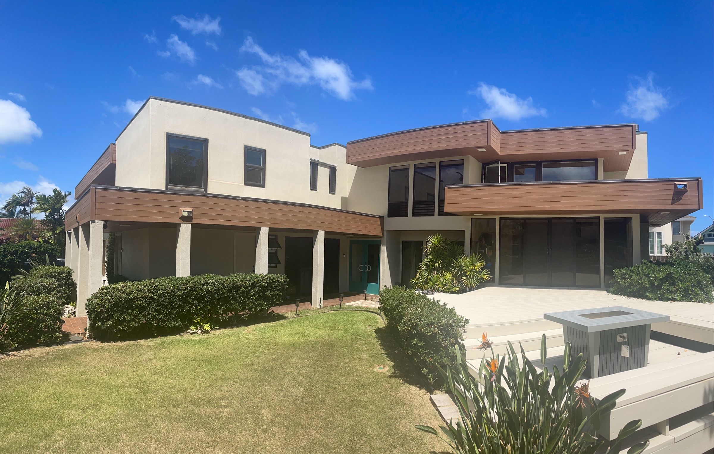 Two-story Oʻahu home in warm-white stucco with wood-tone fascia and teal front doors