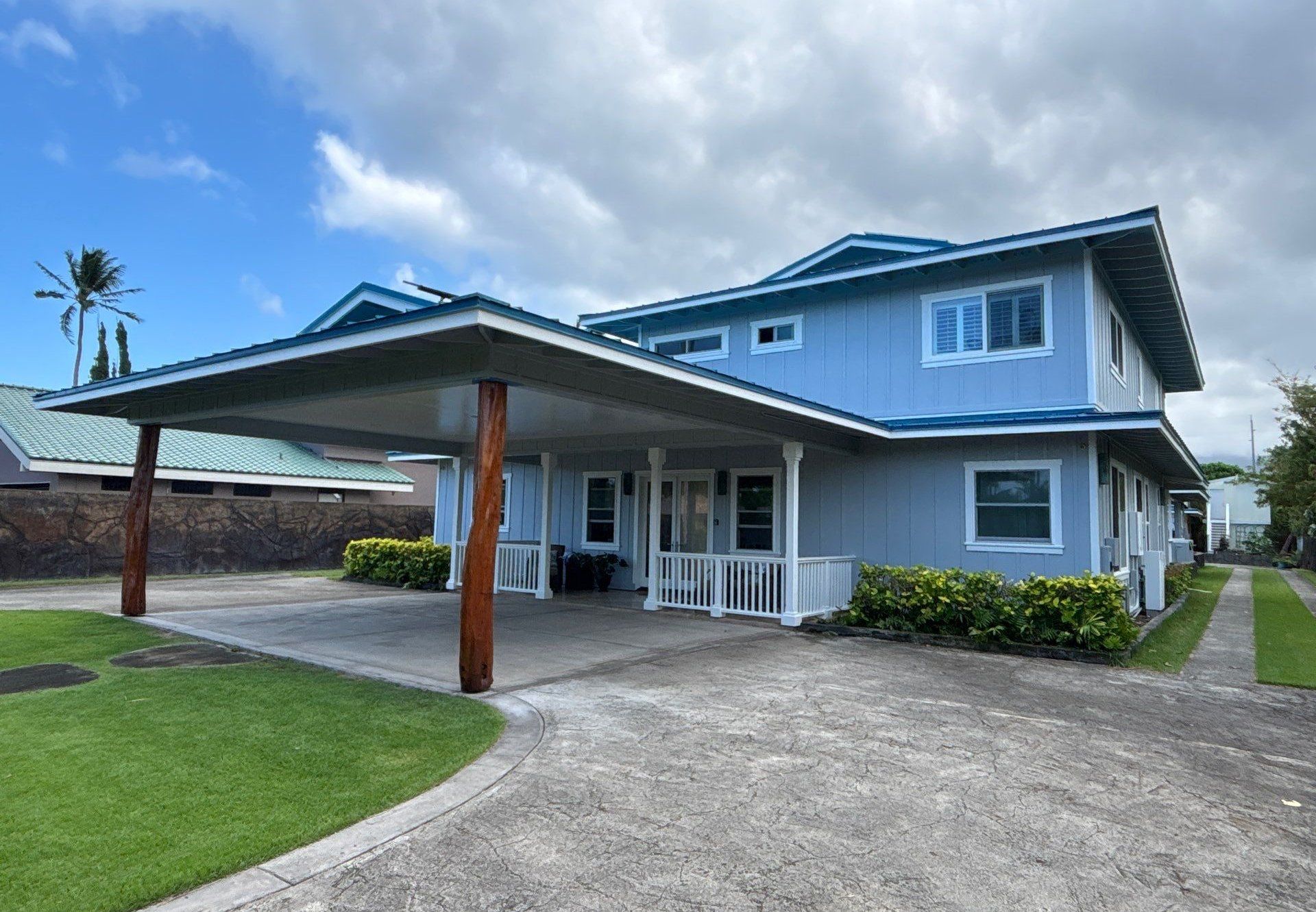 Two-story Kailua home in pale blue board-and-batten with white trim, a white-railed lanai and a carport on natural ʻōhiʻa posts