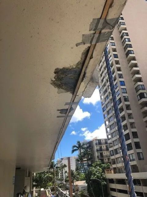 High-rise walkway ceiling with spalled concrete and peeling paint, a neighbouring tower beyond
