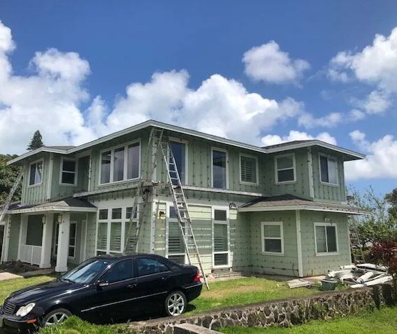 Two-story home in sage green siding with ladders, a sedan parked in front