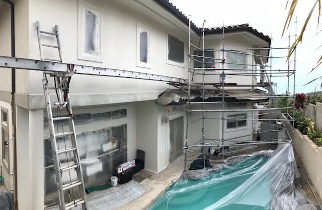 Two-story home under ladders and scaffolding, its pool covered in plastic