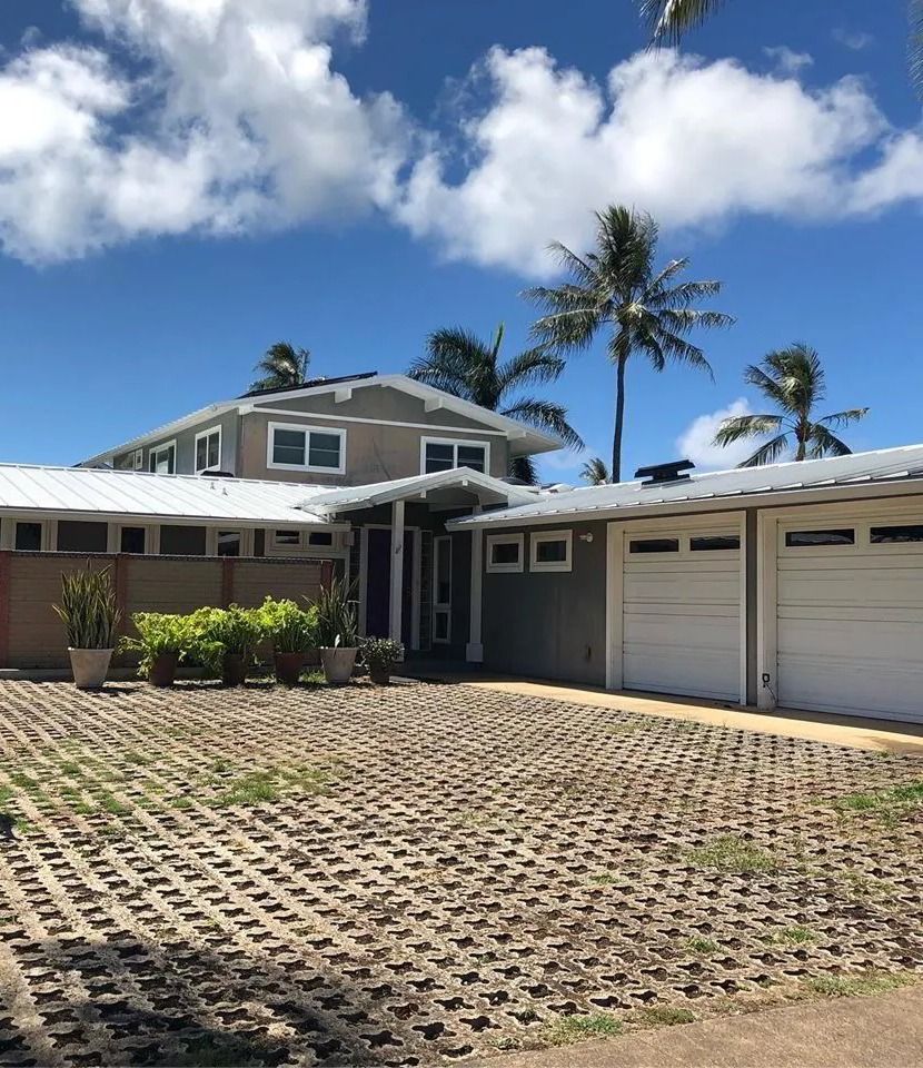 Two-story home in gray-blue siding with white garage doors behind a grass-paver driveway