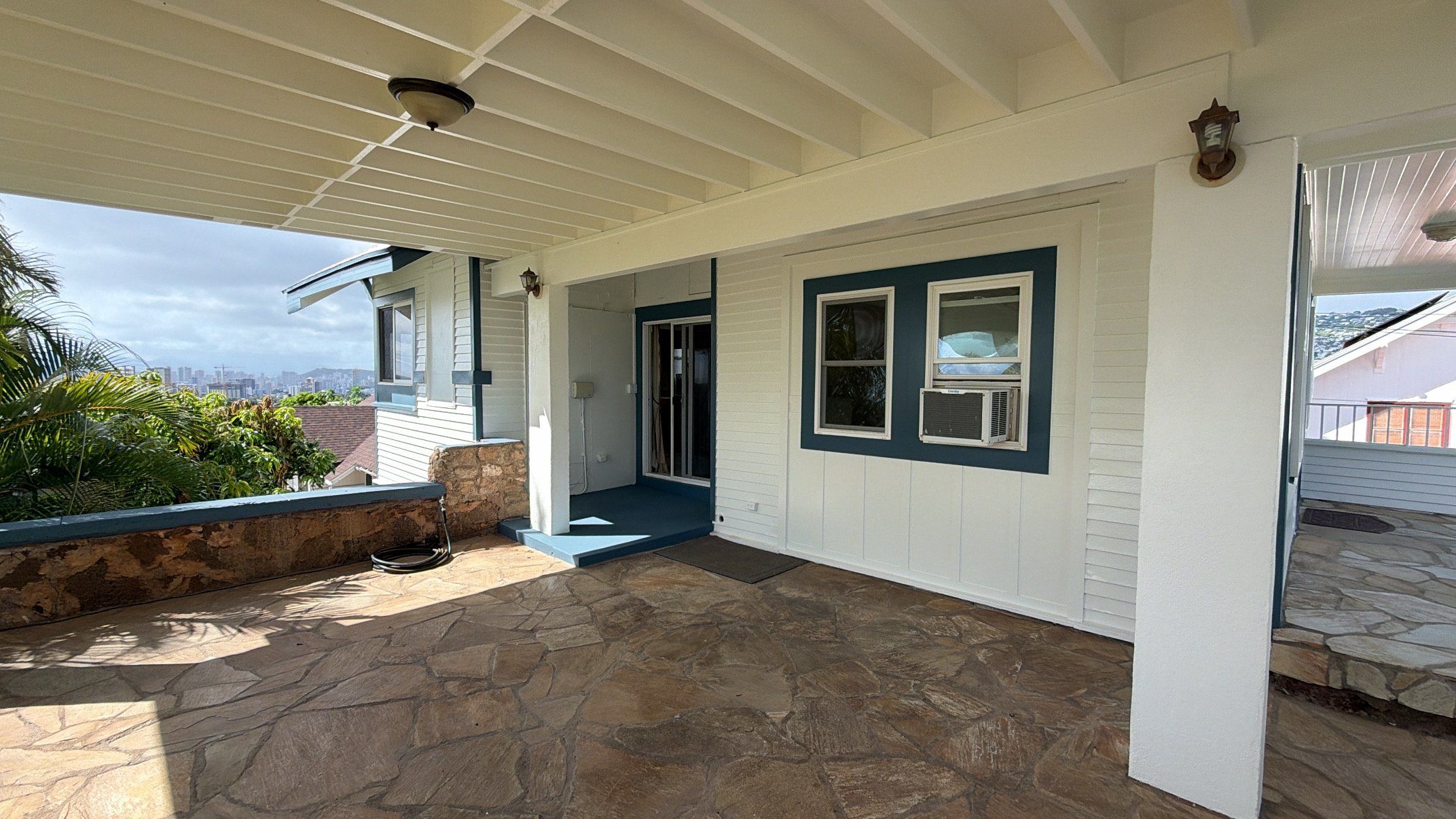 Covered stone lanai of a white home with blue window trim and a city view