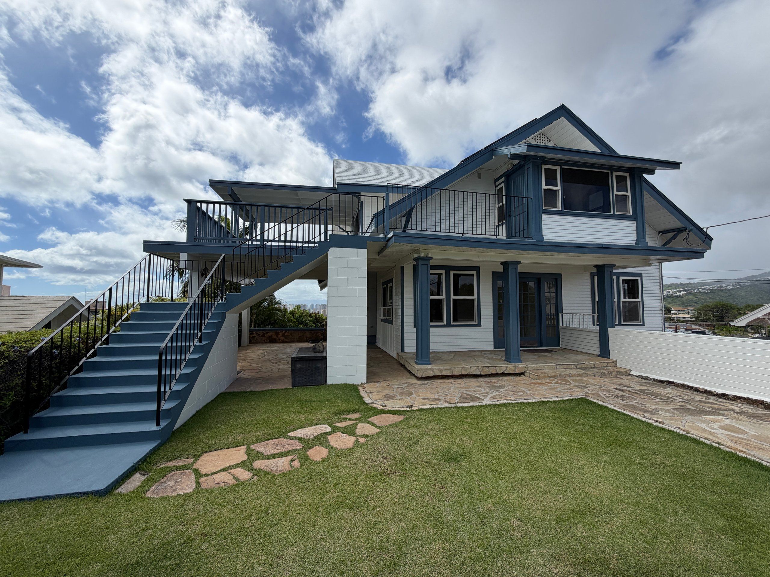 Two-story home in white siding with blue trim, an outside staircase and a stone patio