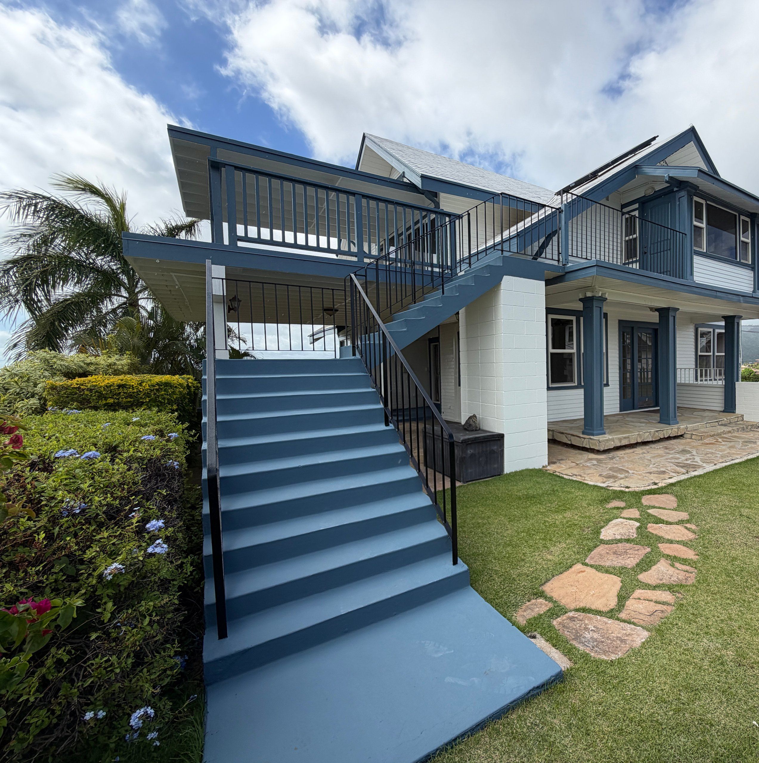 Blue-painted outside staircase rising to the lanai of a white, blue-trimmed two-story home
