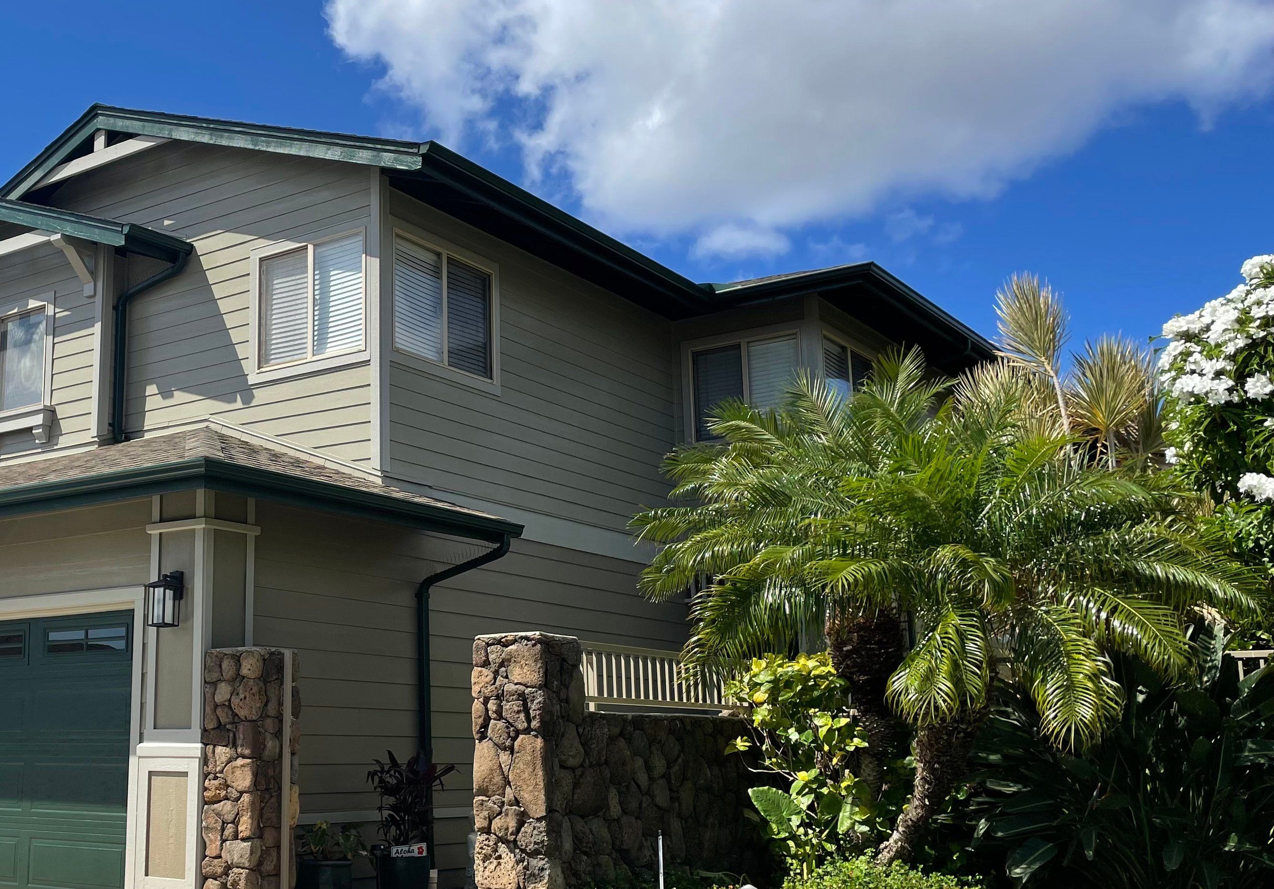 Two-story Craftsman home in sage siding with cream trim, dark green gutters and lava-rock pillars