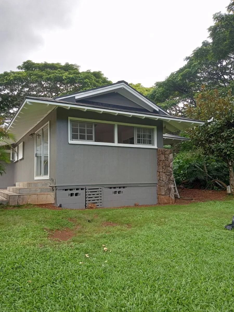 Single-story cottage in gray-green with white trim and a lava-rock pillar