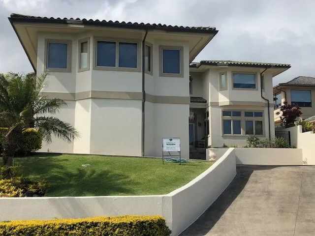 Two-story stucco home in cream with tan bands above a terraced front lawn