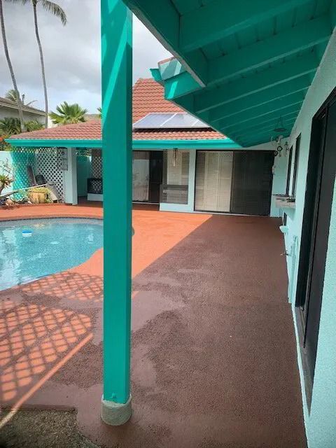 Red pool deck under teal lanai posts, beside a pool and a red-roofed house