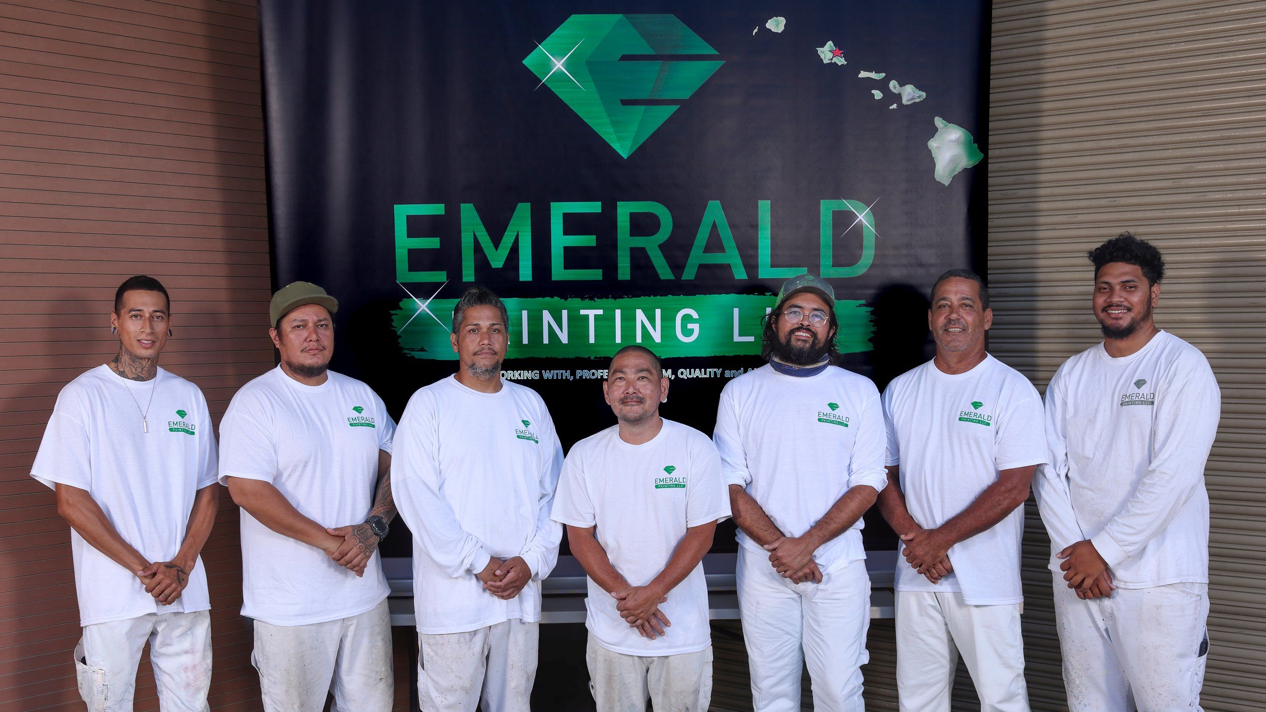 Seven Emerald Painting foremen in white work clothes, standing in front of the company’s banner