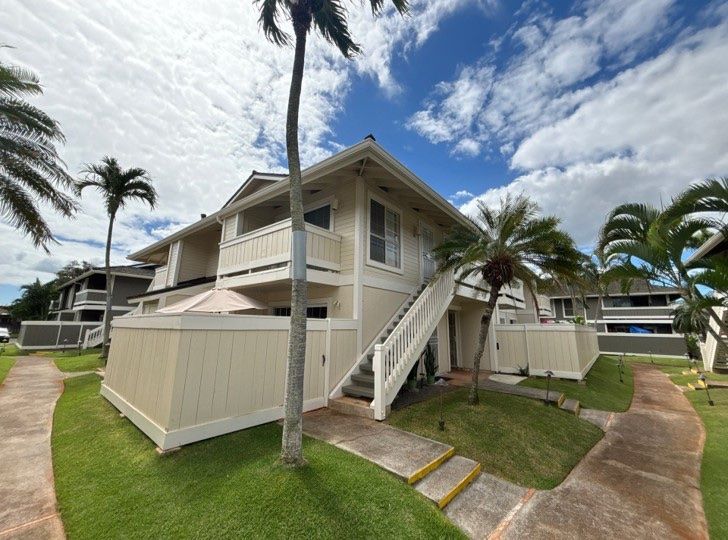 Cream two-story townhome with a white stair rail, among palms